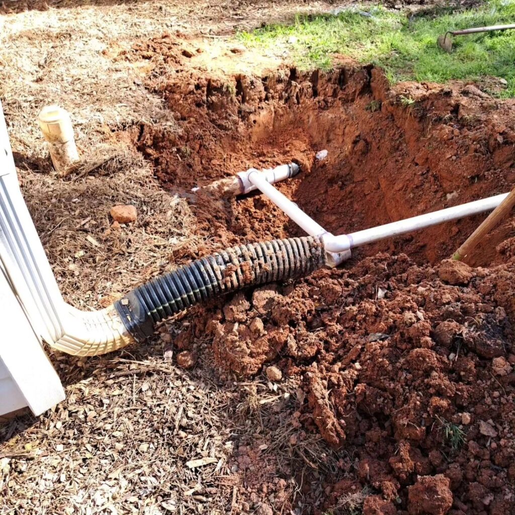 Excavated yard showing PVC pipe and fittings during a plumbing repair